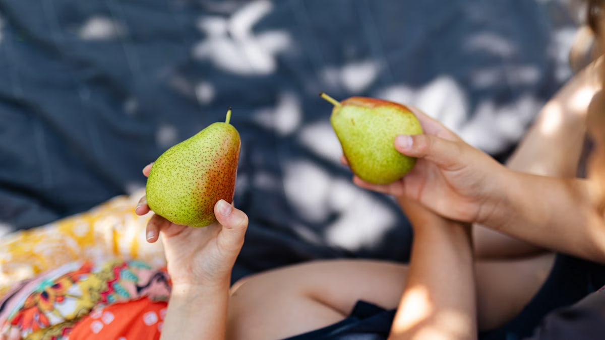 Two children hold ripe pears on a cozy picnic blanket in a sunlit outdoor setting.
